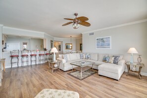 A spacious living room with a large sectional sofa, a dining area with bar stools, and a ceiling fan.