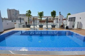 A rooftop swimming pool with a clear blue pool, surrounded by white walls and potted plants.