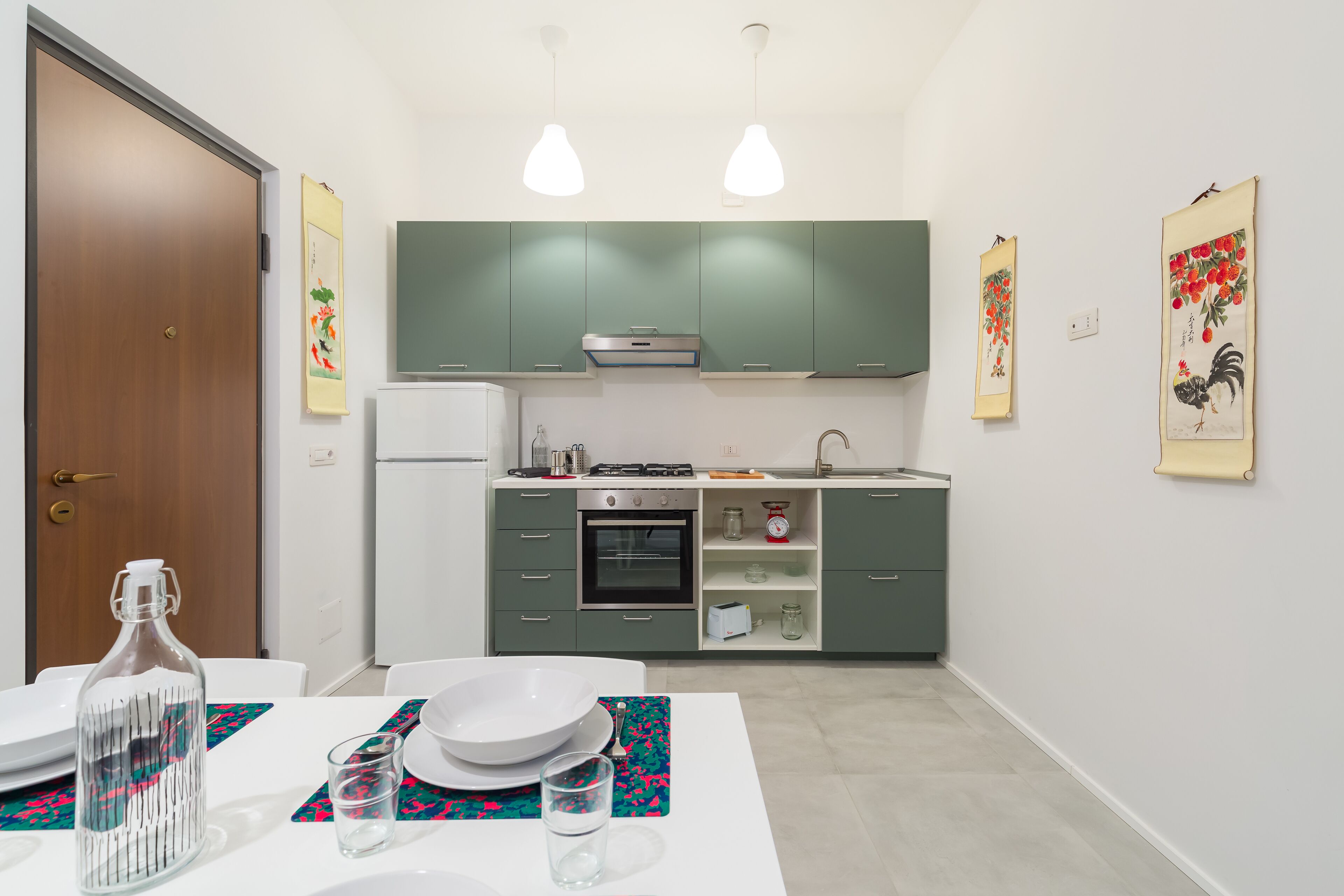 Une cuisine moderne avec des meubles verts, un plan de travail blanc et un coin repas avec une table mise pour deux personnes.
