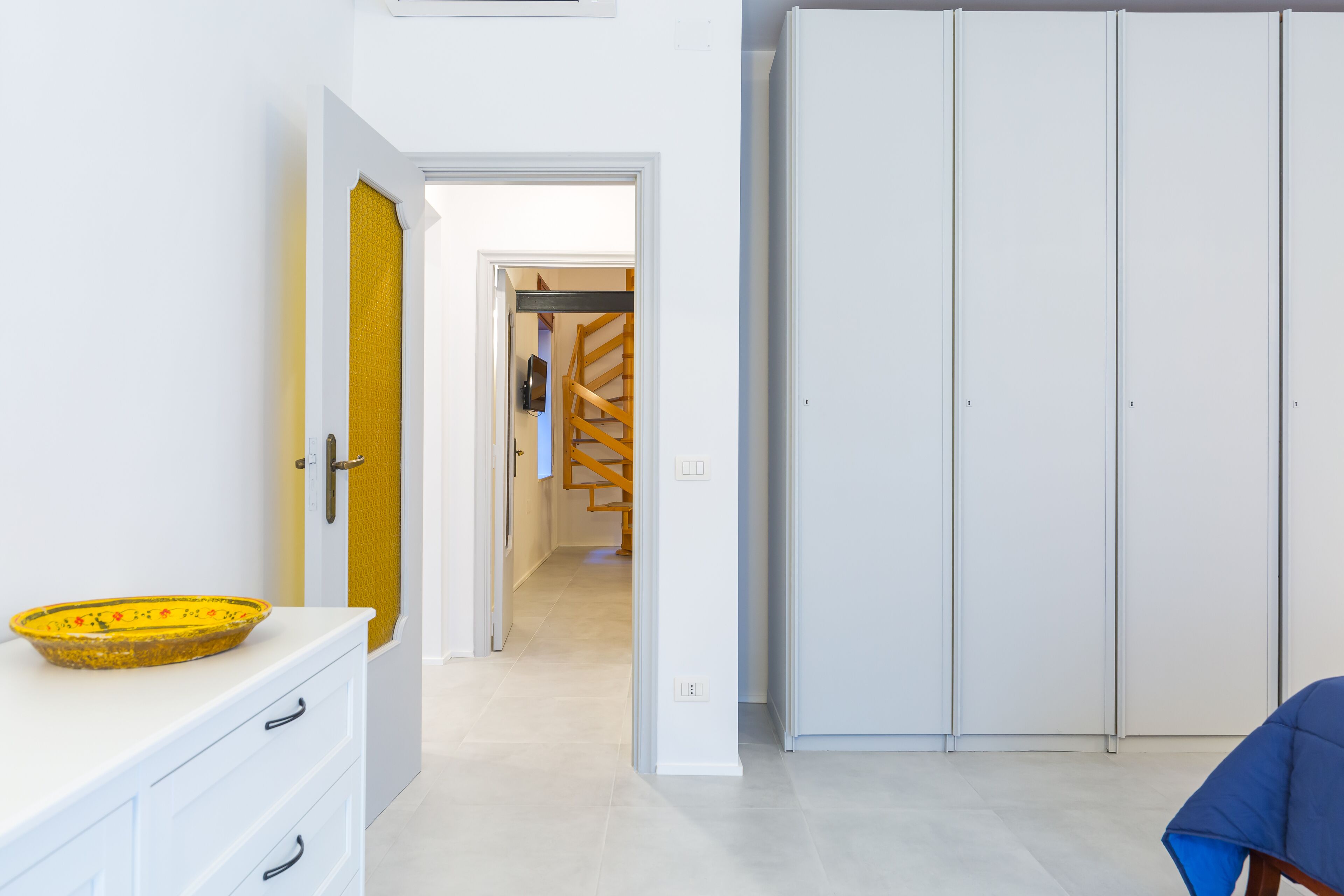 A hallway with a white wardrobe, a yellow door, and a white wall.