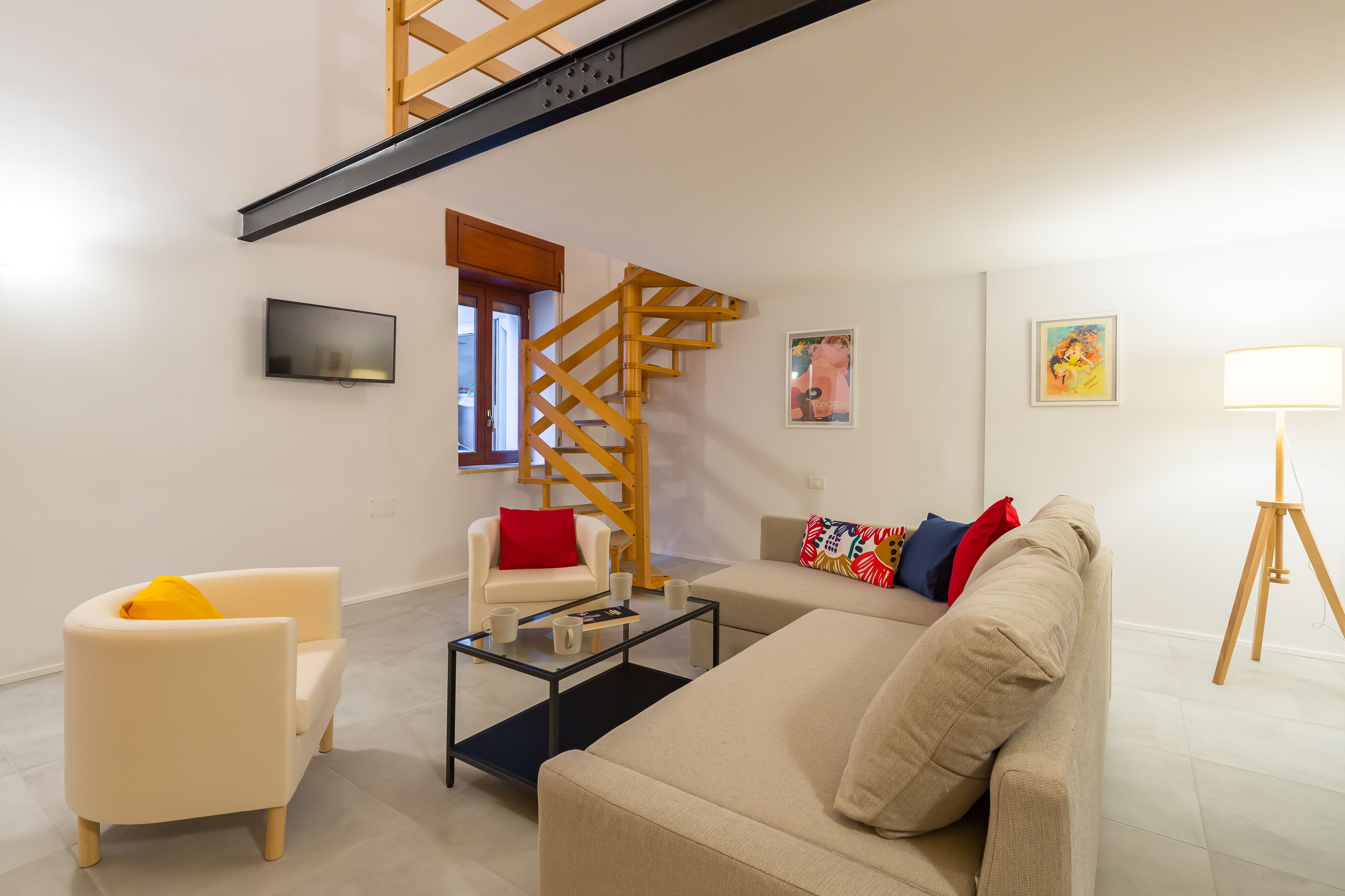 A modern living room with a staircase, a sofa, a chair, a coffee table, and a lamp.