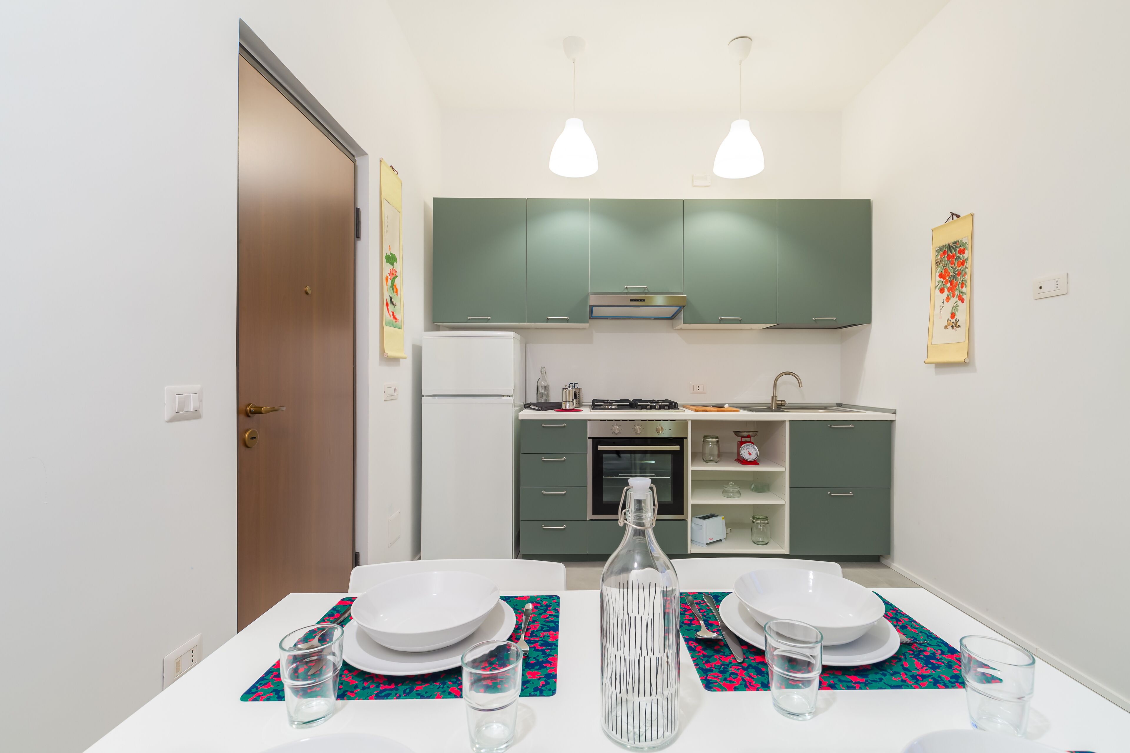A modern kitchen with green cabinets, a white countertop, and a dining area with a table set for two.