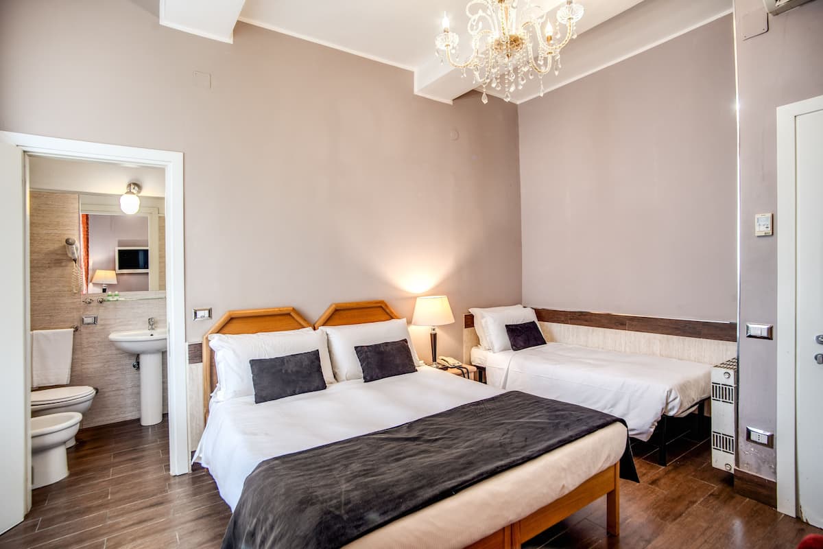 A hotel room with two beds, a bathroom, and a chandelier.