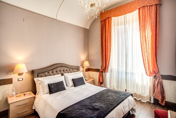 A neatly made bed with a headboard, two bedside tables with lamps, and a window with curtains. - Hotel San Valentino (Rome)