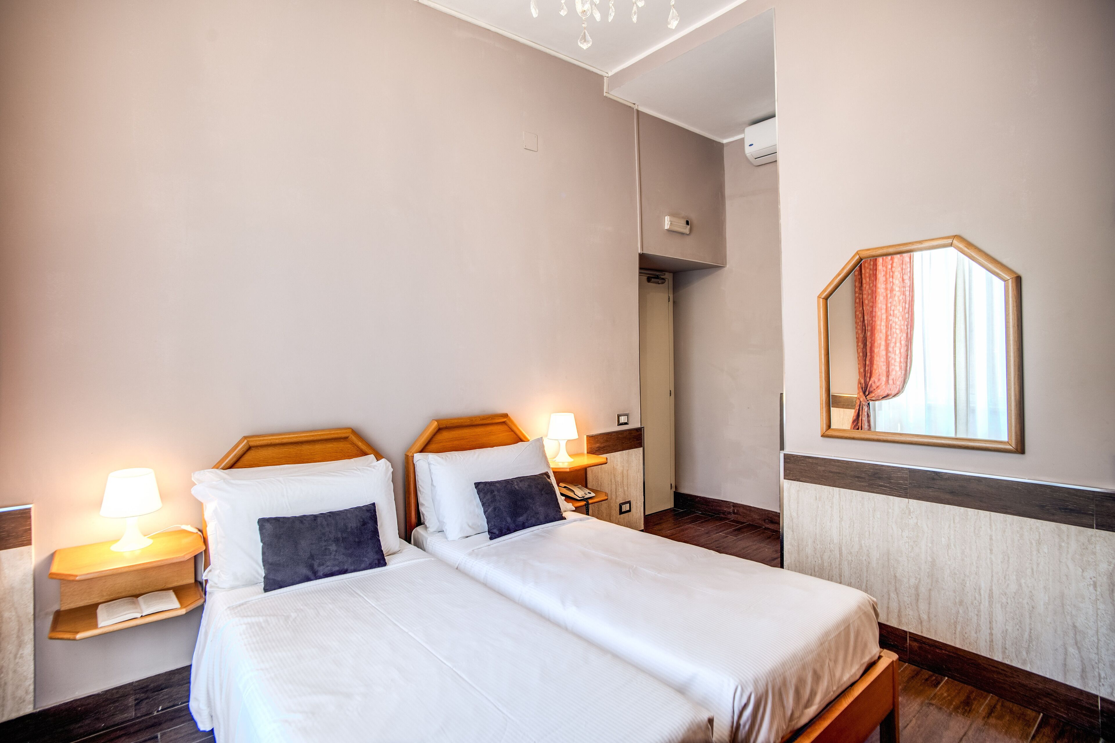Una habitación de hotel con dos camas, lámparas de noche, un espejo y un cabecero de madera.