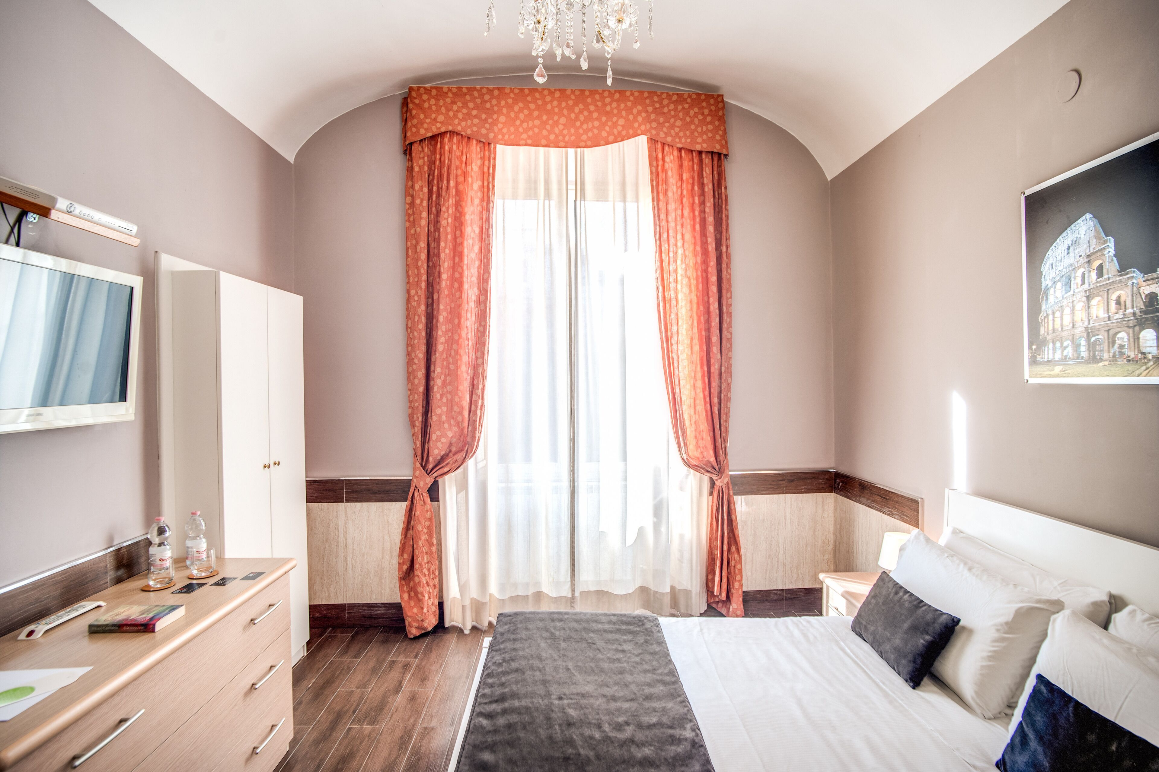 Une chambre d’hôtel avec un lit, un bureau avec un ordinateur, une télévision et une fenêtre avec des rideaux.