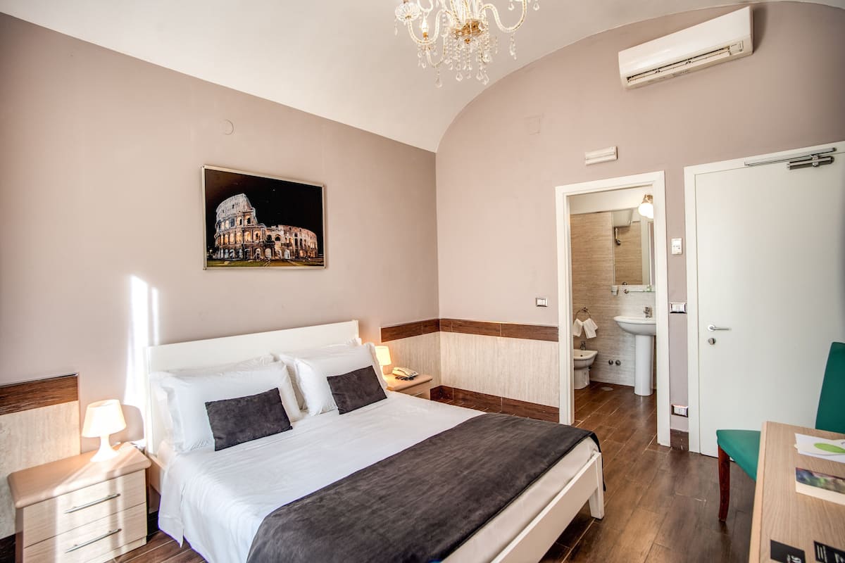 A hotel room with a bed, bedside table, lamp, and a picture of a historical building.