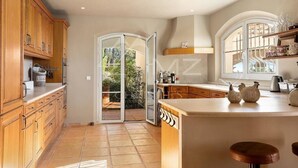 A kitchen with wooden cabinets, a large island, and a sliding glass door leading to a patio. - Beautiful Villa with panoramic seaviews,  easy walking distance to the village (Tourrettes-sur-Loup)