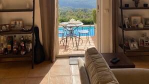 An open doorway leading to a pool area with a view of mountains, a sofa, and shelves with various items. - Beautiful Villa with panoramic seaviews,  easy walking distance to the village (Tourrettes-sur-Loup)