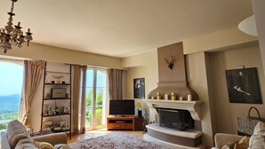 A spacious living room with a fireplace, a television, and a large window overlooking a scenic view. - Beautiful Villa with panoramic seaviews,  easy walking distance to the village (Tourrettes-sur-Loup)