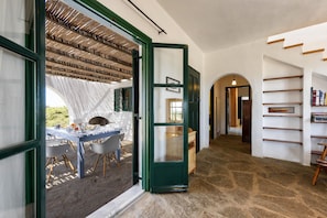 An open doorway leading to a dining area with a table set for two, a stone floor, and a bookshelf with books. - Traditional Villa 5 Mins on Foot From the Beach (Paros)