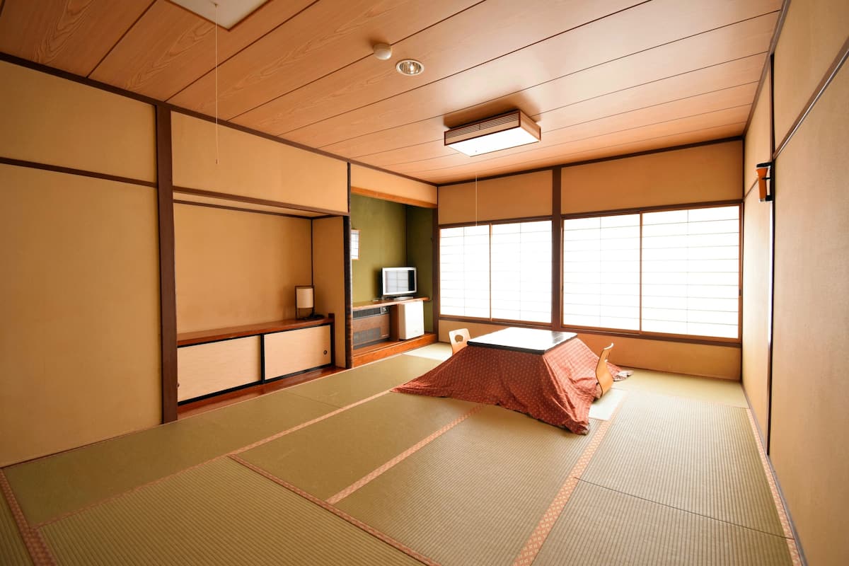 Une pièce de style japonais traditionnel, avec un sol recouvert de tatamis, un futon servant de lit, des portes coulissantes, un téléviseur et une fenêtre ornée de paravents shoji.