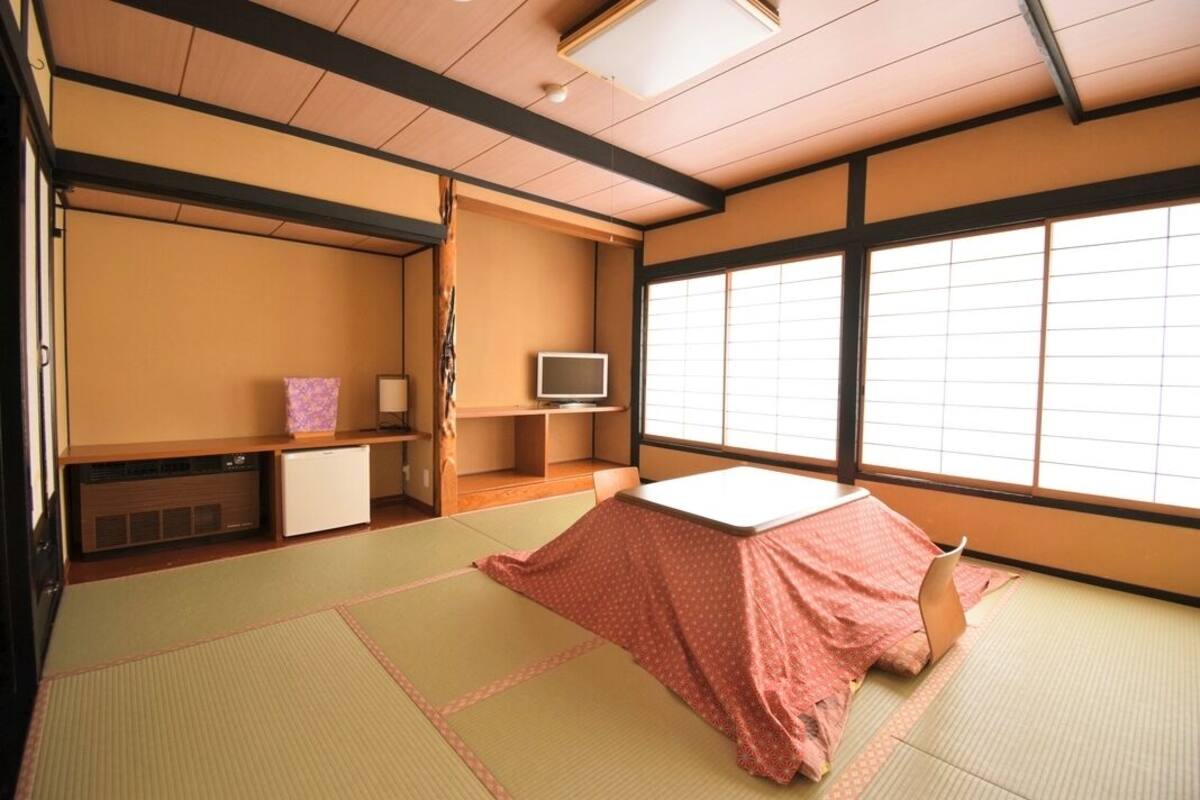 Ein traditioneller japanischer Raum mit Tatami-Bodenbelag, einem Futon und einer Rutschtür sowie einem Fernseher.