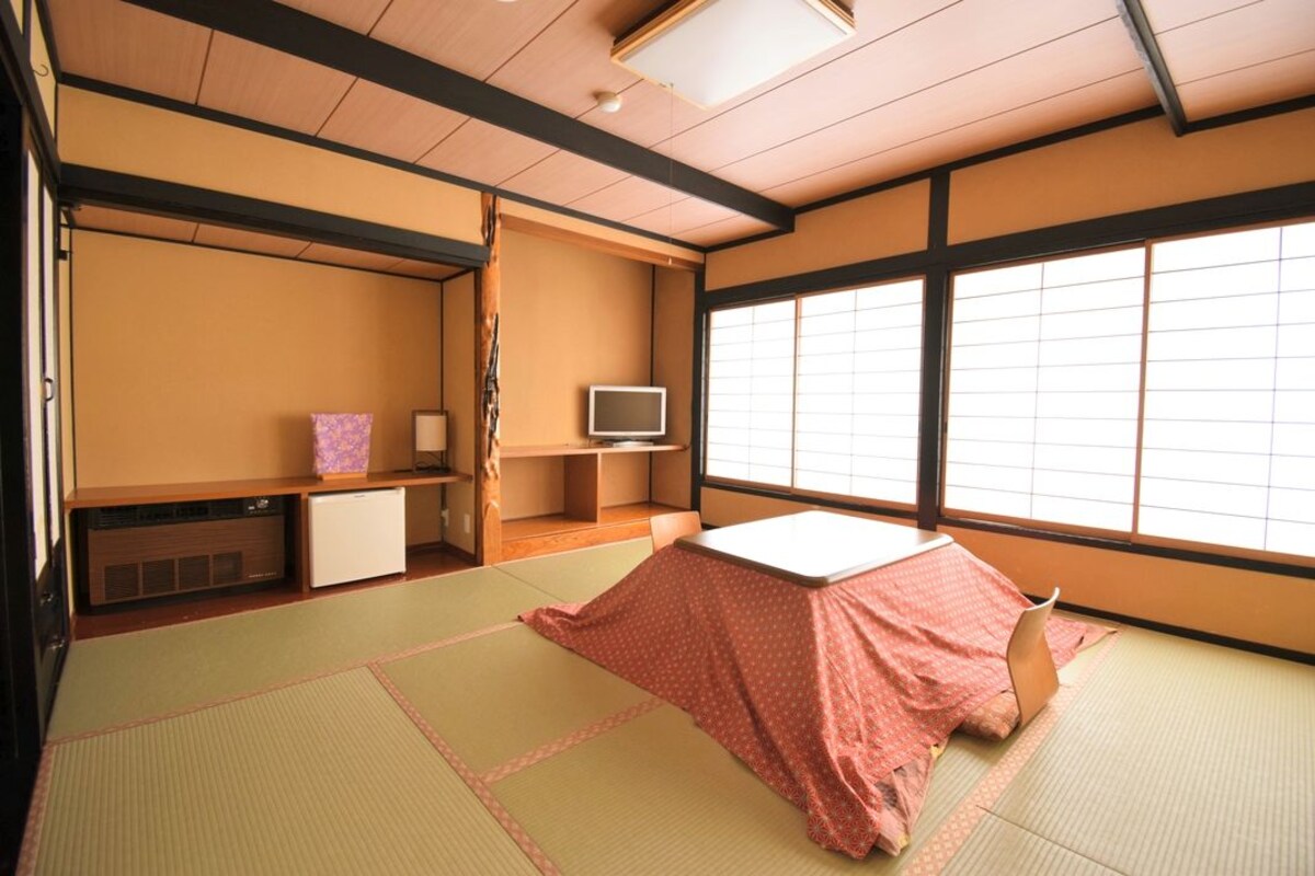 Une pièce de style japonais traditionnel, avec un sol recouvert de tatamis, un futon servant de lit, une télévision et une porte coulissante.