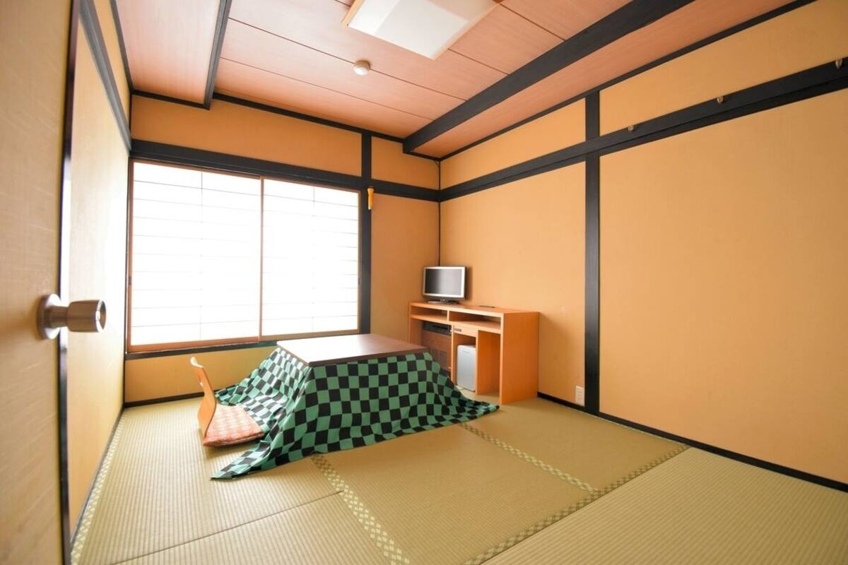 Ein traditioneller japanischer Raum mit Tatami-Bodenbelag, einem Futon, einem Fernseher und einer Schiebetür.