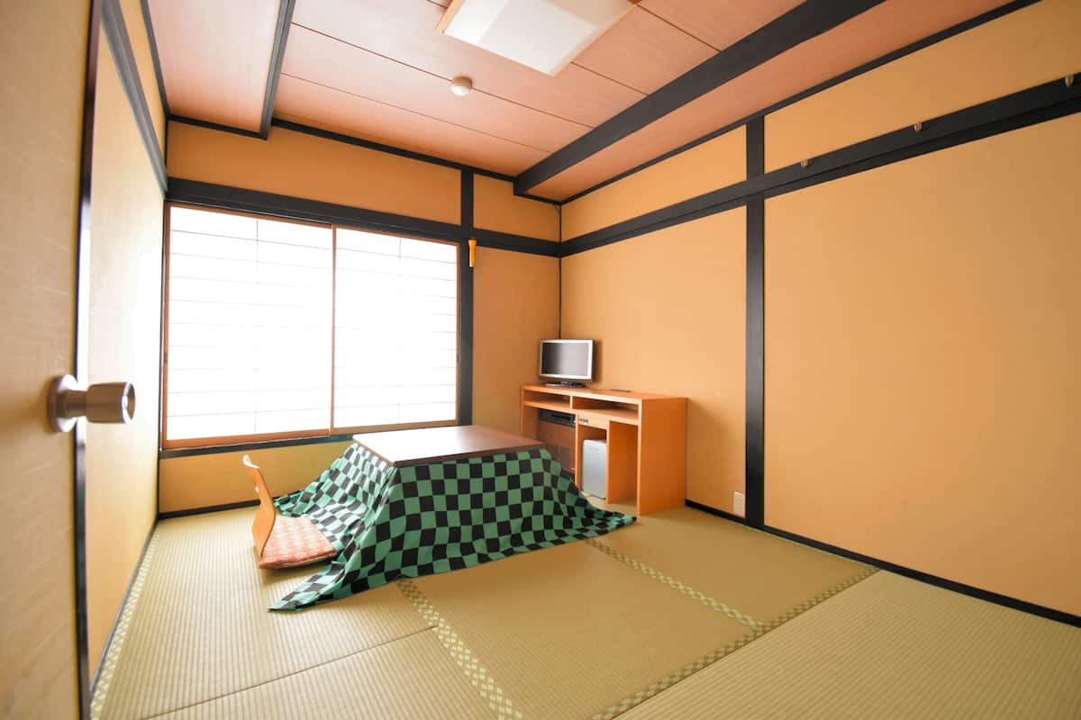 Ein Raum mit Tatami-Matten, einem Futonbett, einem Fernseher auf einem Holzboden und einer Schiebetür.