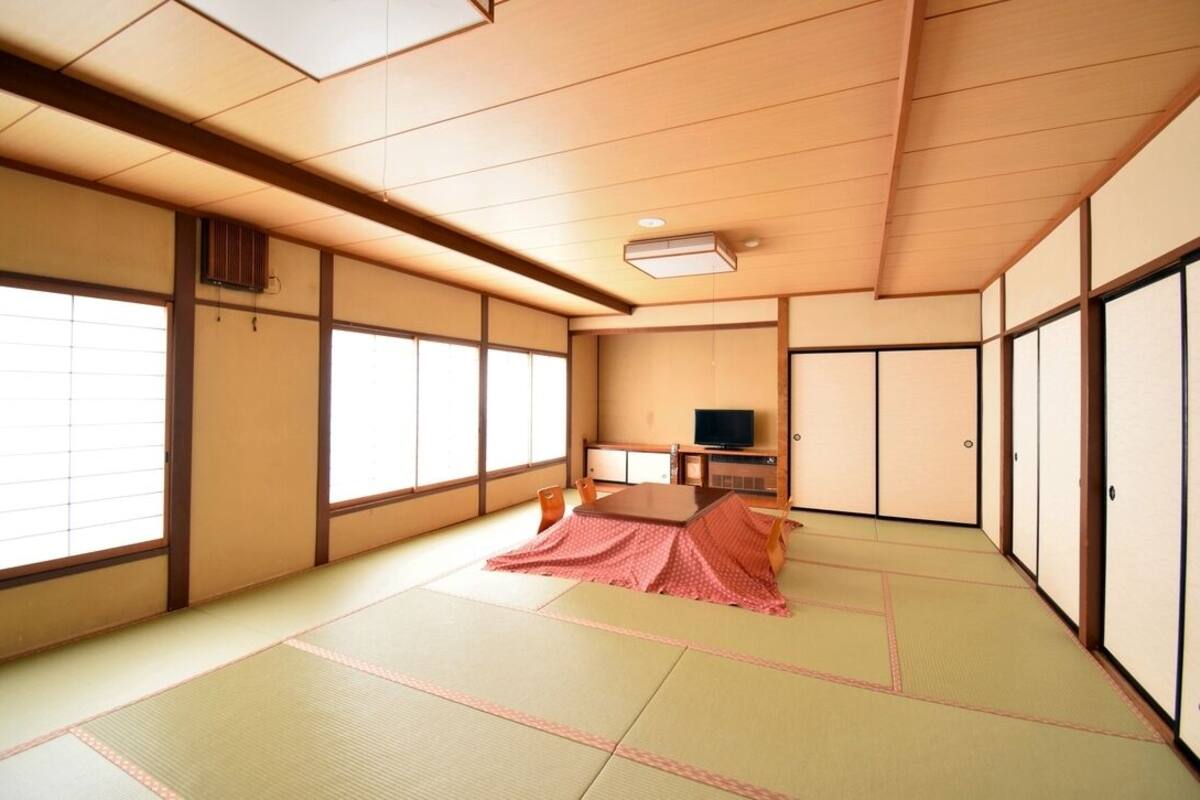Ein traditioneller japanischer Raum mit Tatami-Boden, Schiebetüren, einem Fernseher und einem Futon.