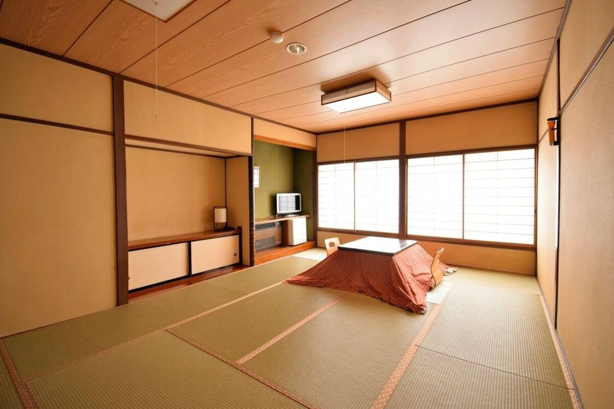 Ein traditioneller japanischer Raum mit Tatami-Böden, einem Futon und einer Fernseher, sowie Schiebetüren.