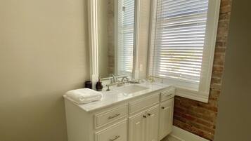A bathroom with a double sink vanity, a large mirror, and a window with blinds.