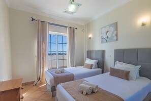 Ett hotellrum med två sängar, ett stort fönster, en tavla och ett skrivbord i trä.