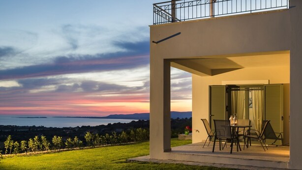 Une maison moderne dotée d’un balcon donnant sur un espace verdoyant et offrant une vue sur le coucher de soleil.