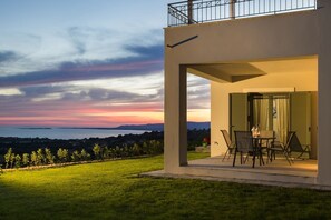 Een modern huis met een balkon met uitzicht op een gazon en een zonsondergang.
