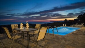 Un espace aménagé au bord de la piscine, avec une table et des chaises, une piscine et une vue sur le coucher de soleil.