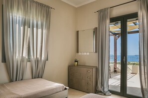 A bedroom with a bed, a dresser, a mirror, and a view of the sea through a sliding glass door.