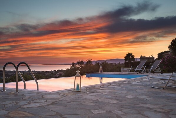A poolside area with lounge chairs and a view of a sunset over a body of water.