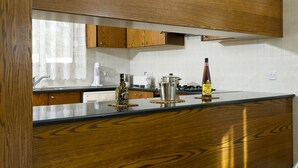A kitchen with wooden cabinets, a stainless steel sink, and a countertop with a bottle of Metaxa. - Luxury villa on mountainside with sea views (Kathikas)