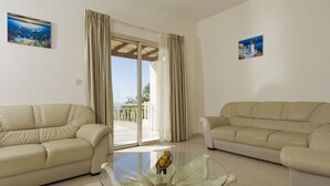 A living room with two beige sofas, a glass coffee table, and a balcony with curtains. - Luxury villa on mountainside with sea views (Kathikas)