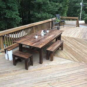 Enjoy meals and relaxation on the deck with a table and benches surrounded by lush greenery.