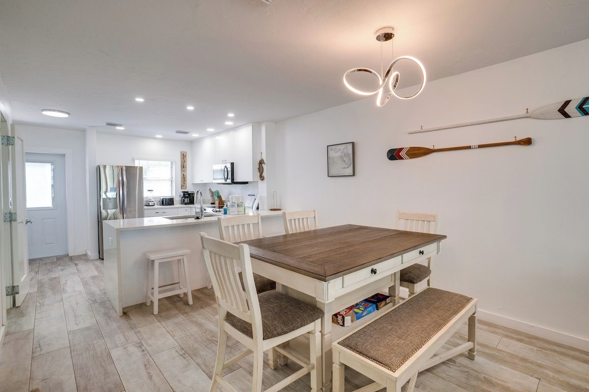 Een moderne keuken met witte kasten, een centraal keukenblok en een eetgedeelte met een houten tafel en witte stoelen.