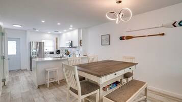 Een moderne keuken met witte kasten, een centraal keukenblok en een eetgedeelte met een houten tafel en witte stoelen.