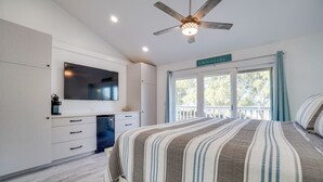 Quarto com cama, ventoinha no teto, televisão e janela com cortinas.
