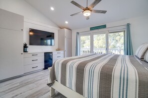 A bedroom with a bed, a ceiling fan, a TV, and a window with curtains.