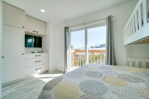 A bedroom with a bed, a TV, a balcony, and a view of the outside.