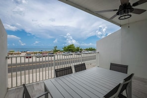 A balcony with a table and chairs, overlooking a beach with parked cars and a road.