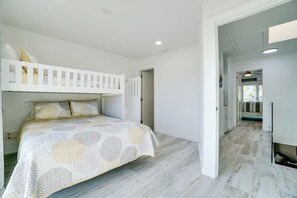 A bedroom with a bunk bed, a large bed with a patterned bedspread, and a hallway leading to a bathroom.