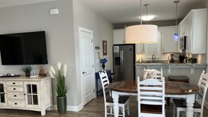 Une cuisine moderne avec des meubles blancs, un grand réfrigérateur et un coin repas comprenant une table en bois et des chaises blanches.