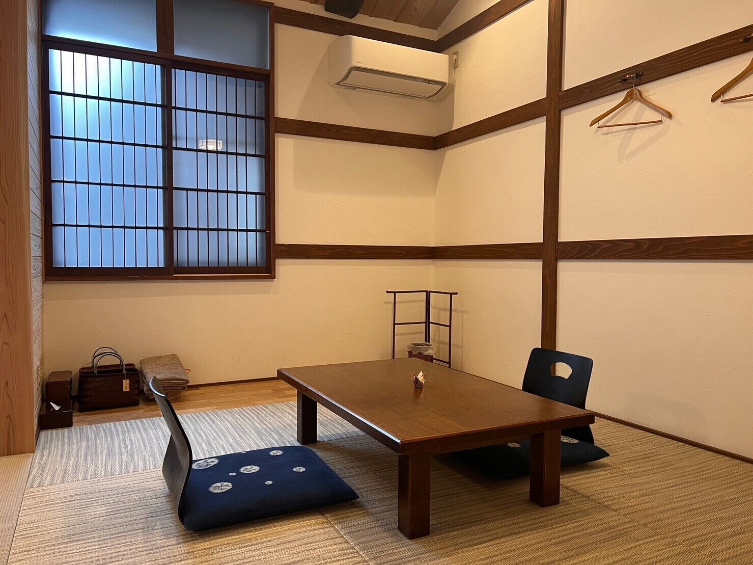 A traditional Japanese room with tatami flooring, a low table, a bench, and a sliding door with glass panels.