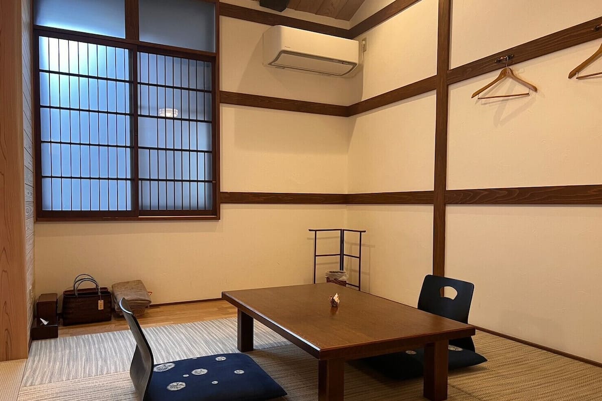 A traditional Japanese room with tatami flooring, a low table, a bench, and a sliding door with glass panels.