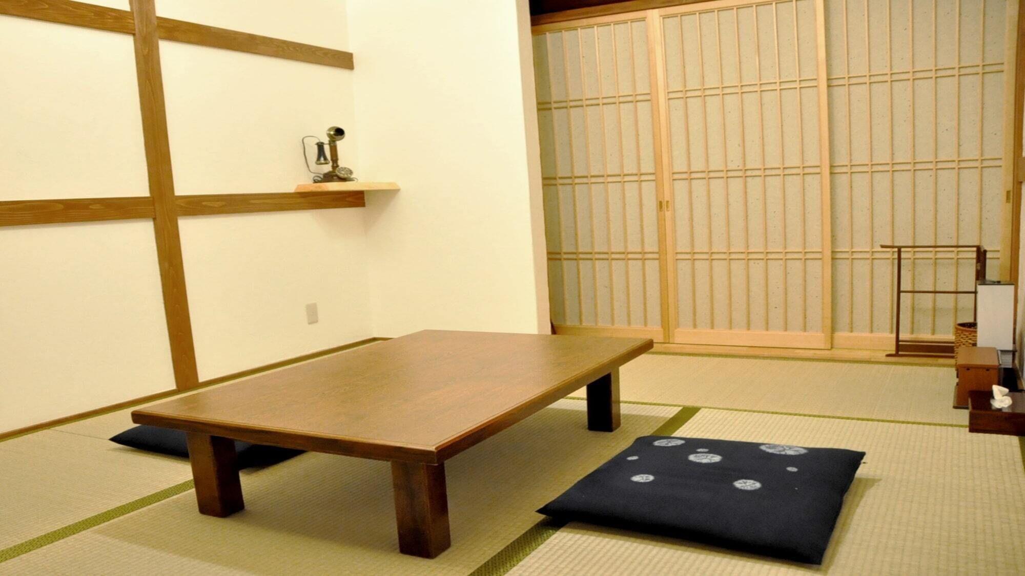 A tatami mat room with a low wooden table, a shoji screen, and a small shelf with a decorative item.