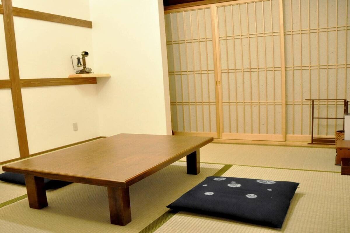 A tatami mat room with a low wooden table, a shoji screen, and a small shelf with a decorative item.