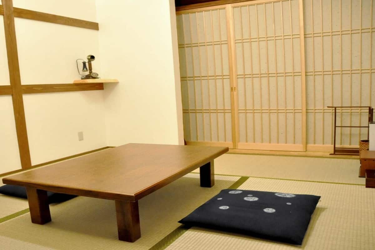 A tatami mat room with a low wooden table, a shoji screen, and a small shelf with a decorative item.