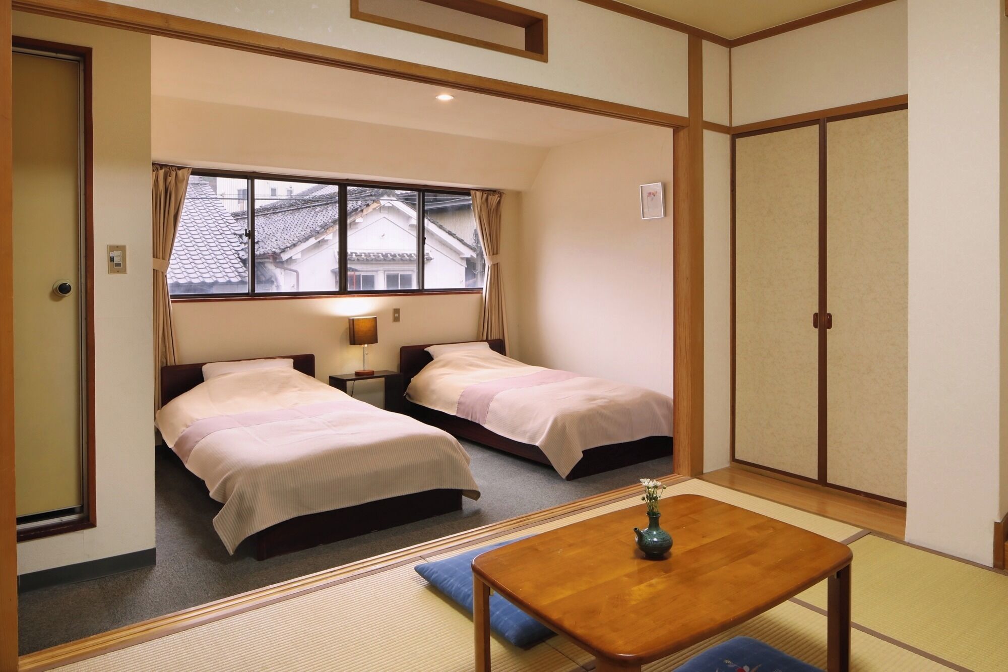 A hotel room with two beds, a small table, and a window with curtains.