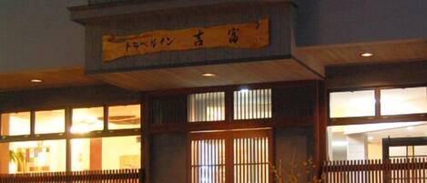 Un edificio japonés tradicional con entrada de madera, un letrero sobre la puerta y vista del interior a través de las ventanas.