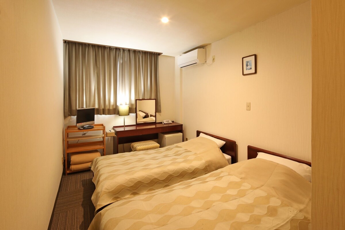 A hotel room with two beds, a desk with a computer, a lamp, and an air conditioning unit.