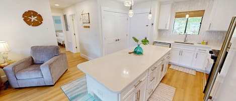 A modern kitchen with white cabinets, a central island, and a dining area with a grey sofa.