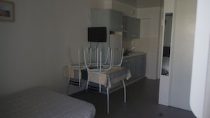 Una habitación pequeña y escasamente amoblada con cama, escritorio, silla, televisor y armario.